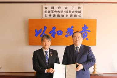 太子町の田中 祐二町長(左)と、須原 祥二学長(右) ＝ 12月15日(木)、背景の「以和為貴」は17条憲法の第1条「和を以て貴しとなす」